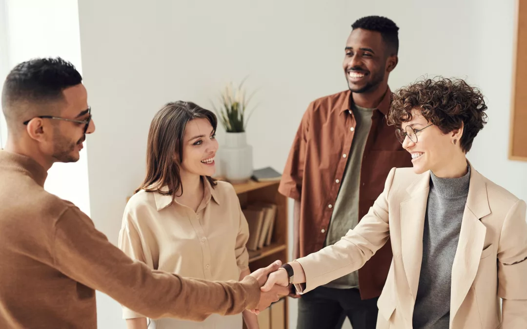 Groupe de collègues souriants se serrant la main lors d’une rencontre professionnelle dans un bureau moderne